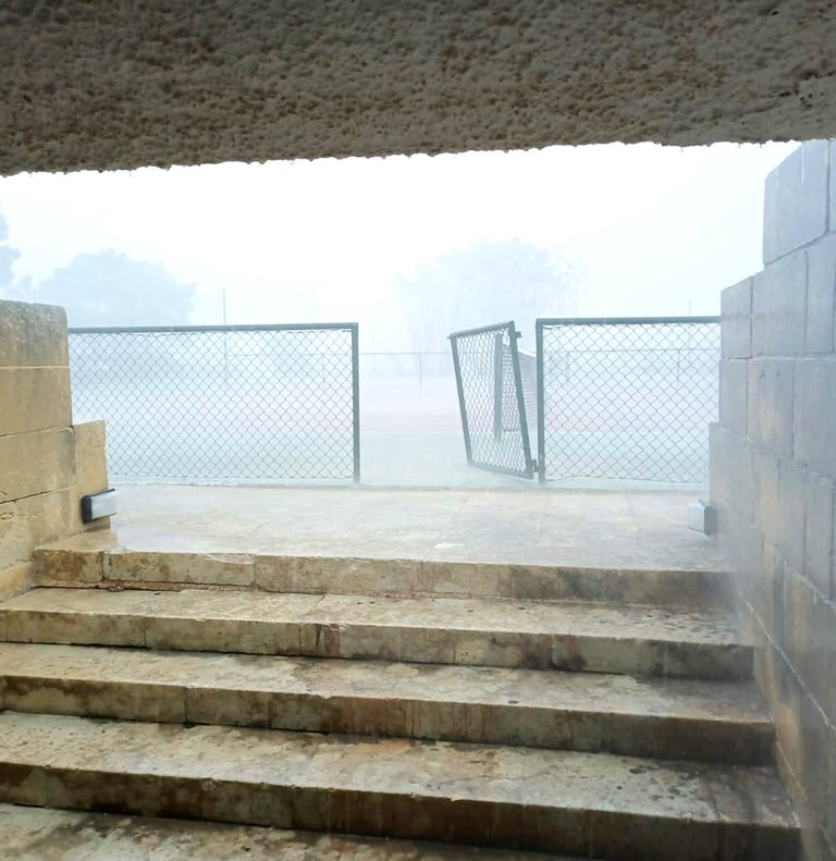 Rainy stone steps leading to a foggy outdoor sports court with a chain link fence gate.