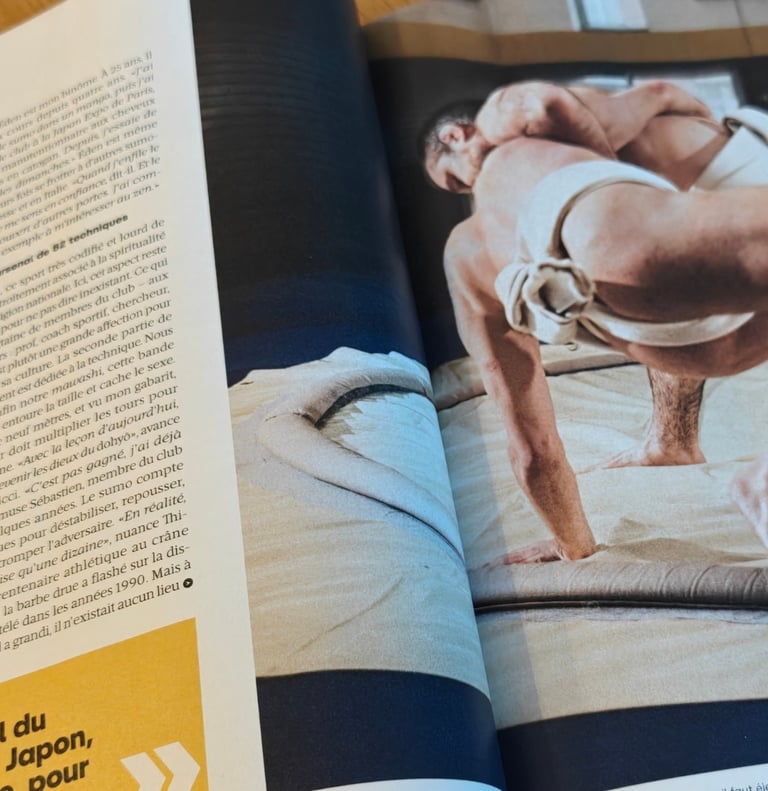 Photo d'un magazine avec sur la page de droite 2 hommes en mawashi, dont l'un a la main au sol suite a une clé de bras