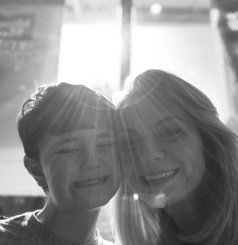 Black and white portrait of a smiling mother and son with bright sunlight creating lens flares.