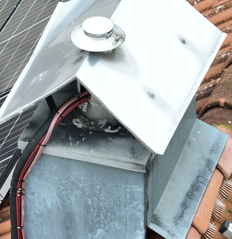 drone picture of a stainless steel chimney cap and vent installed on a tiled roof near solar panels.