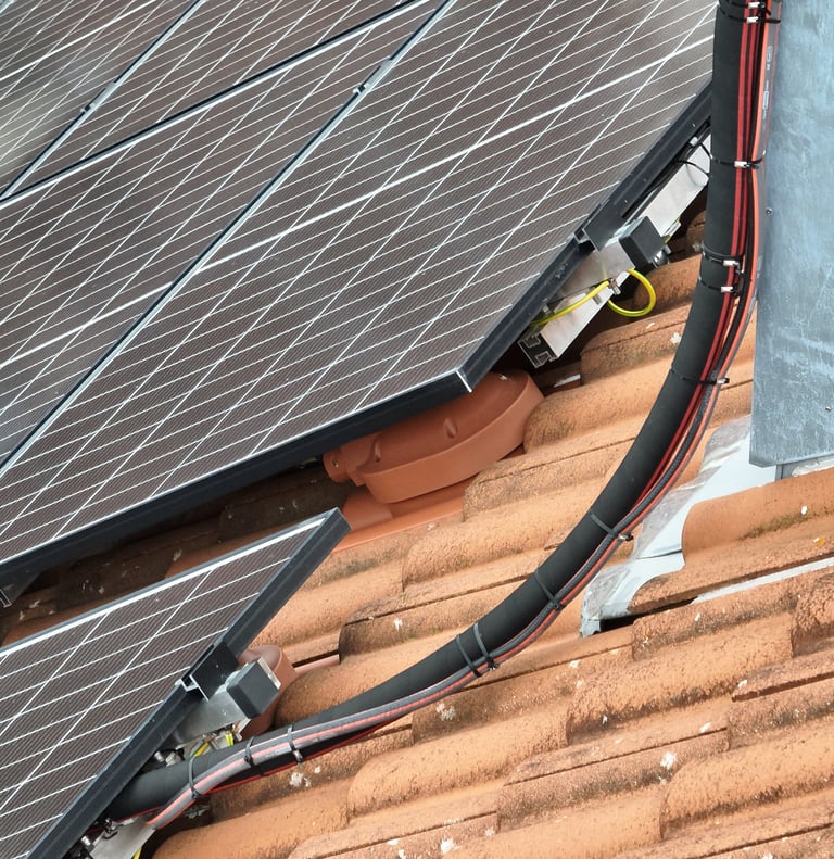 Close-up of residential solar panels installed on a clay tile roof with visible electrical wiring and mounting brackets.