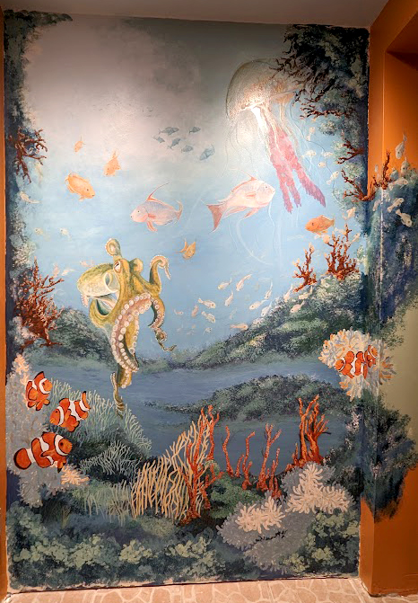 An active, life filled colorful coral reef of fish, octopus, and jelly fish wall mural by Kathy LaFollett.