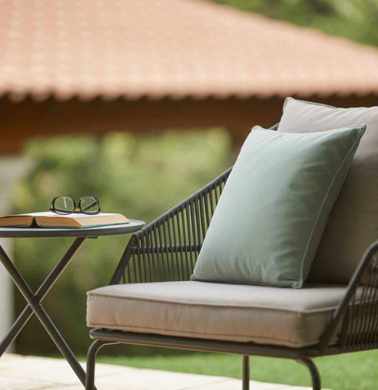 Modern outdoor lounge chair with cushions next to a side table with a book and glasses.
