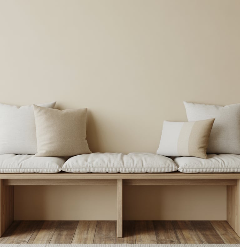 A simple bench placed along a wall with cushions, a small stack of books beside it, clean surroundin