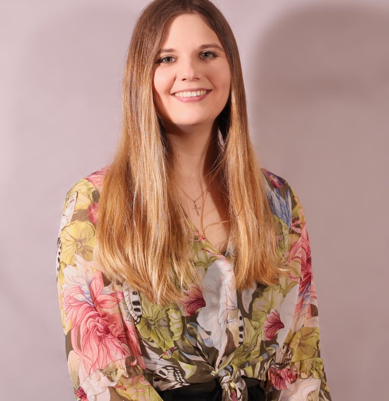 A professional headshot of Care-iss with long hair and a flowery blouse smiling at the camera.