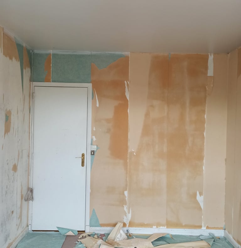 Une pièce en cours de rénovation montrant des murs avec du papier peint arraché, des débris sur le s