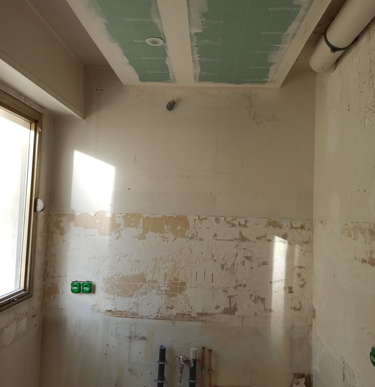 Rénovation de cuisine en cours avec tuyaux de plomberie apparents, plafond en placo et câblage 