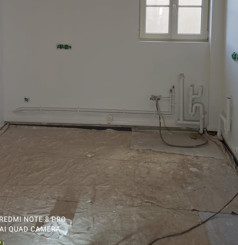 Une cuisine en cours de rénovation avec des tuyaux de plomberie apparents, des prises électriques et