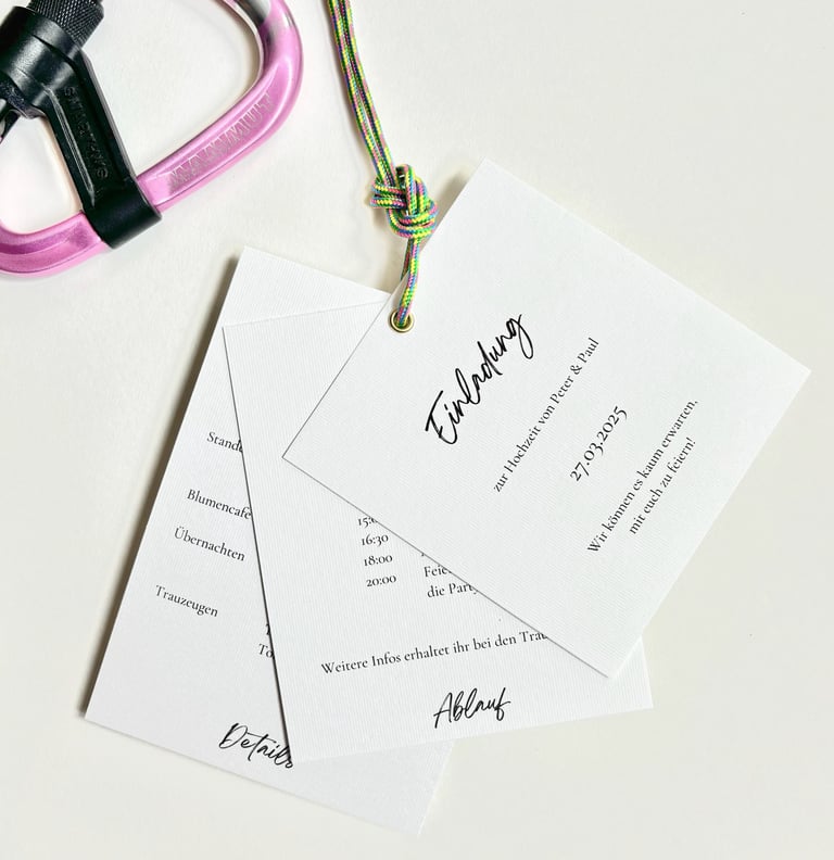 eine schlichte Hochzeitseinladung, bestehend aus mehreren Seiten. Sie wird durch eine Öse und ein Kl