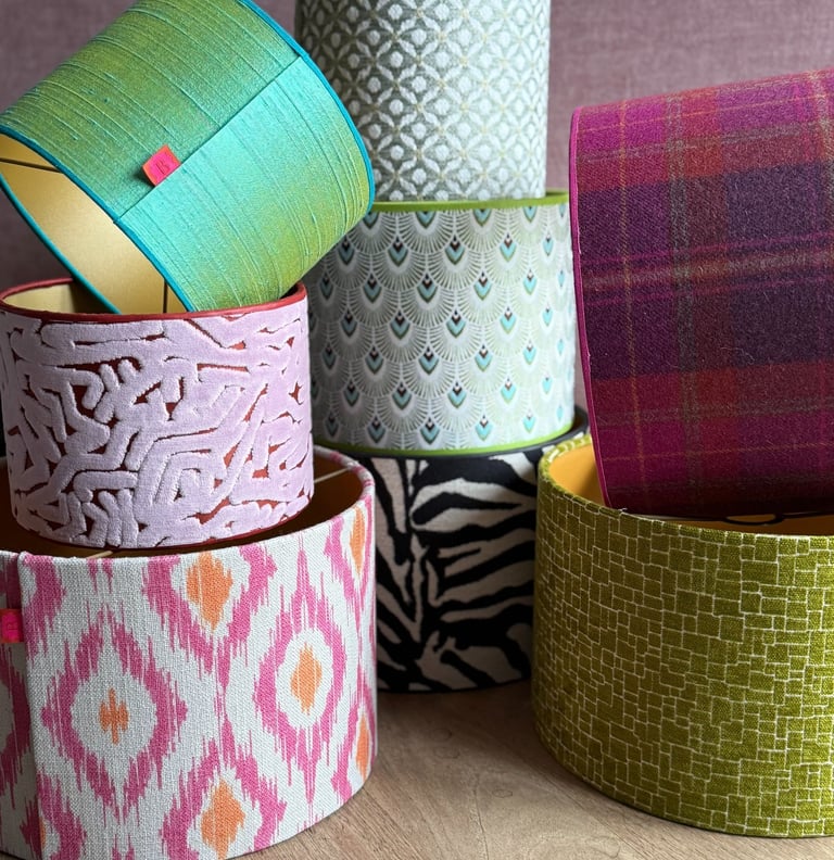 A colorful stack of decorative drum lampshades featuring ikat, plaid, and animal print fabrics.