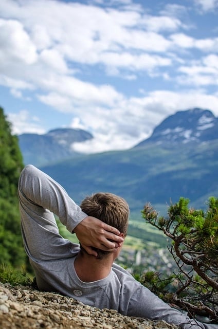 Homme allongé en montagne main gauche derrière la tête regardant un haut sommet un peu enneigé