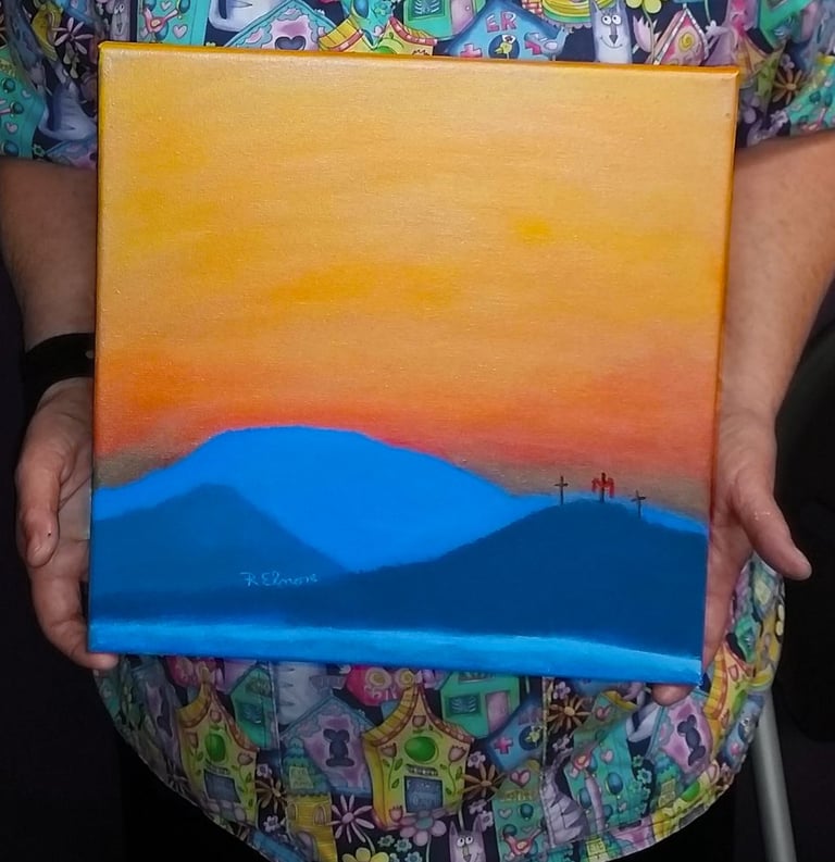 a woman holding a painting of a mountain scene with three crosses