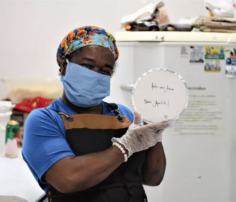 Voluntária da ONG Misturaí segurando uma das marmitas produzidas e distribuidas a população carente 