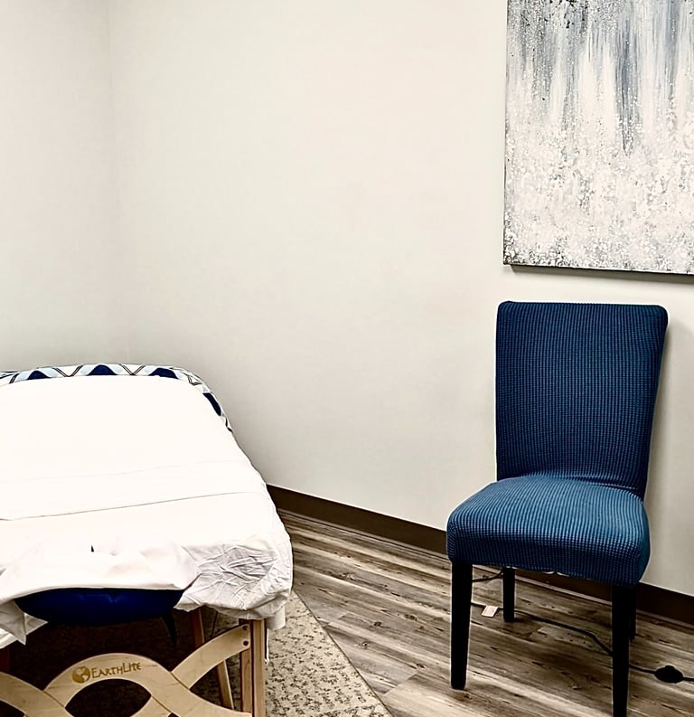 Professional massage therapy room featuring an Earthlite table, a blue chair, and abstract wall art.