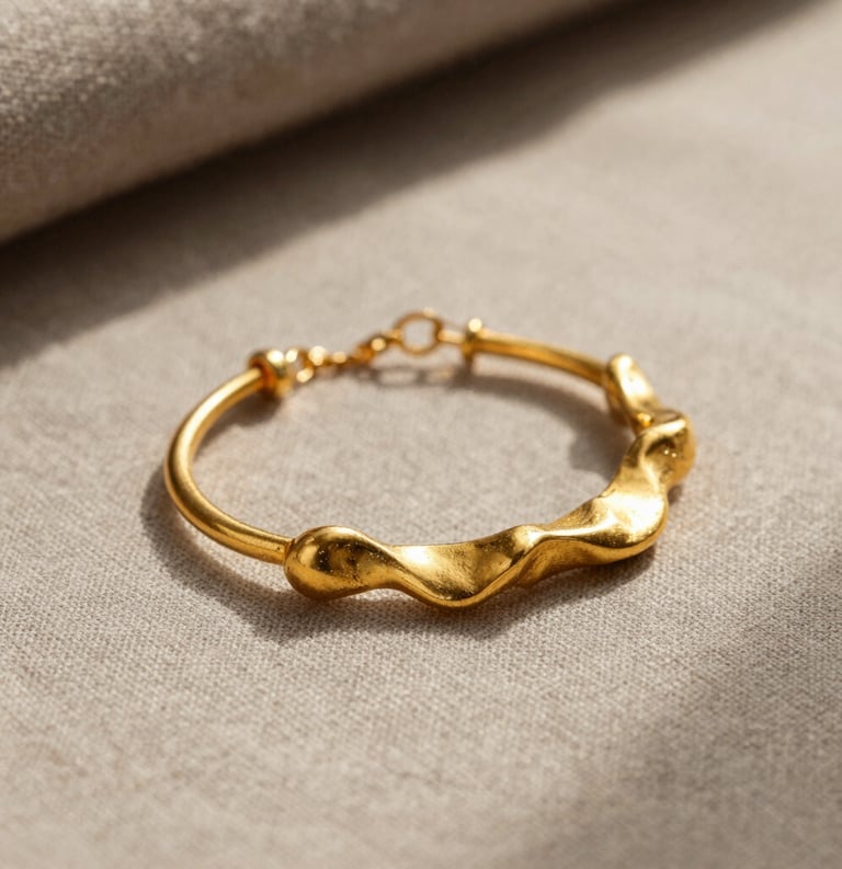 A professional close-up photograph of handcrafted gold jewelry featuring organic shapes, resting on a soft taupe linen surface in a North American studio with warm, diffused sunlight.