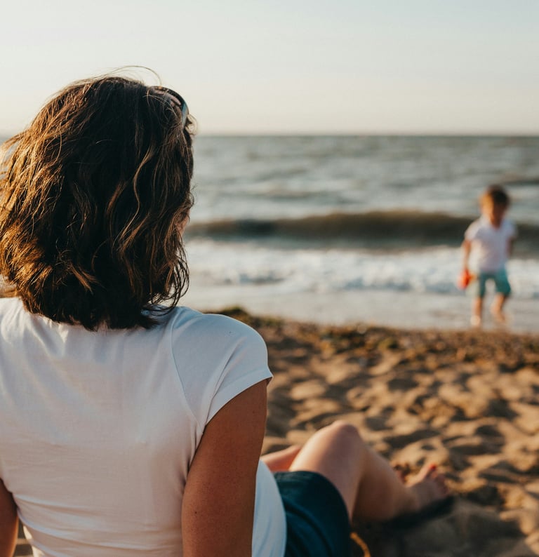 Mère assise sur la plage, face à la mer, regarde son fils jouer au bord de l'eau