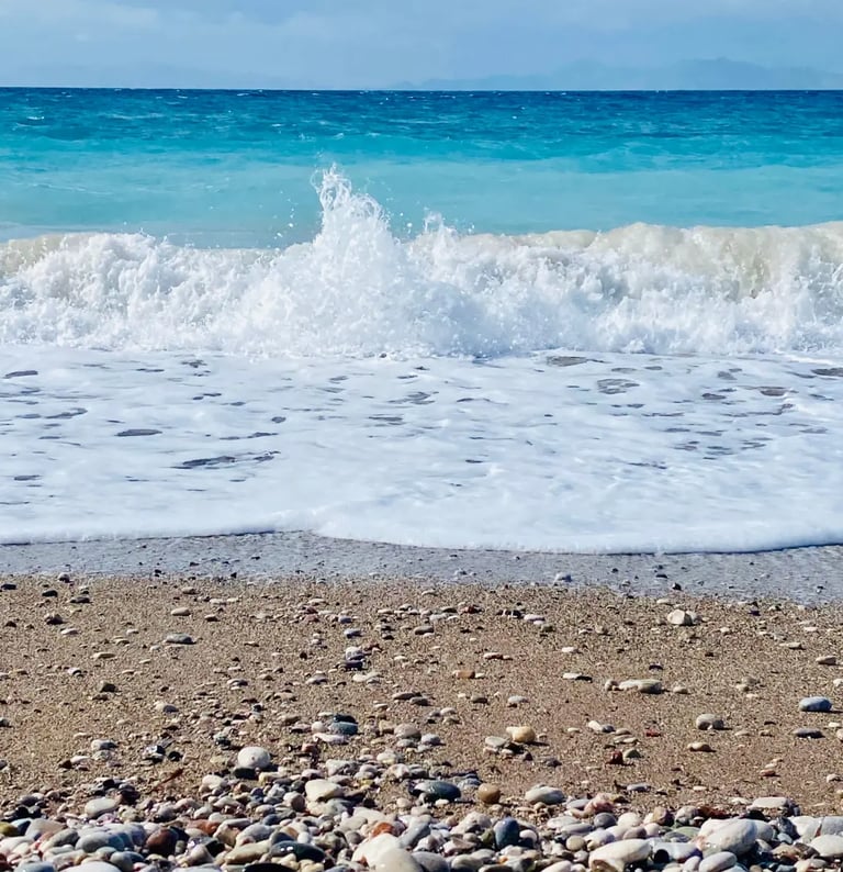 Turquoise ocean waves crashing on a pebbled sandy beach under a clear blue sky.