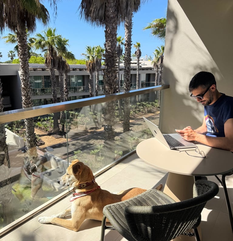 Venture Along co-founder working on a laptop with his dog on a balcony overlooking palm trees.