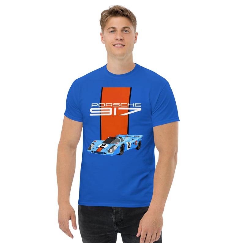Un homme blond et musclé avec un t-shirt PORSCHE 917 bleu et orange.