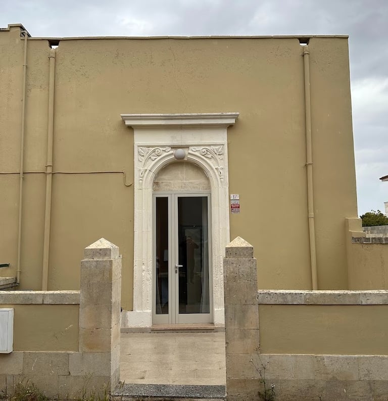 Minimalist beige building facade with an ornate white stone arched doorway and glass entry door.