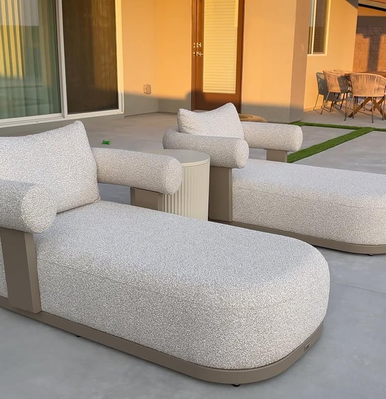 Modern outdoor chaise lounges with curved gray upholstery on a luxury concrete patio at sunset.