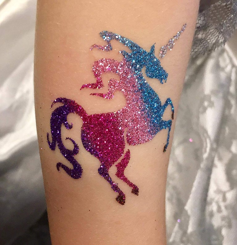 a unicorn glitter tattoo on a woman's arm