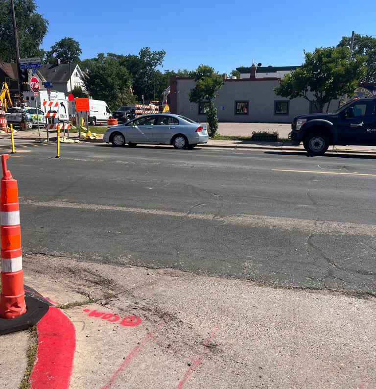 Silver sedan on George Floyd Square construction zone with orange cones and utility trucks.