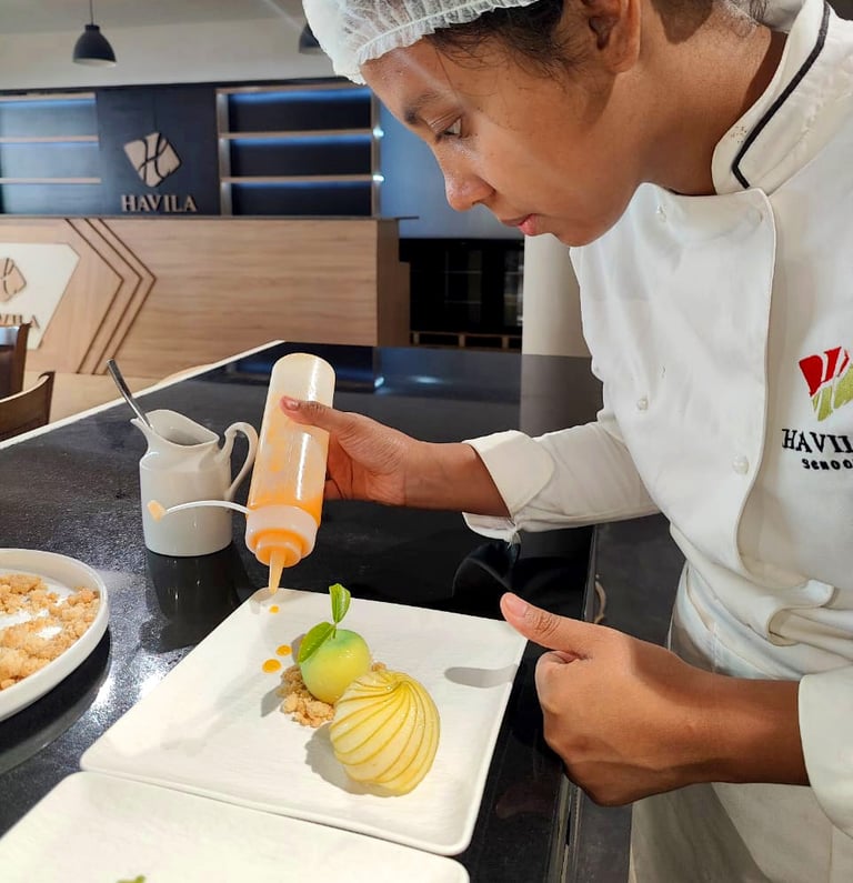 a chef in a white uniform is pouring a sauce on a plate