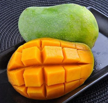 Fresh whole green mango and a sliced mango half cut into cubes on a black plate.