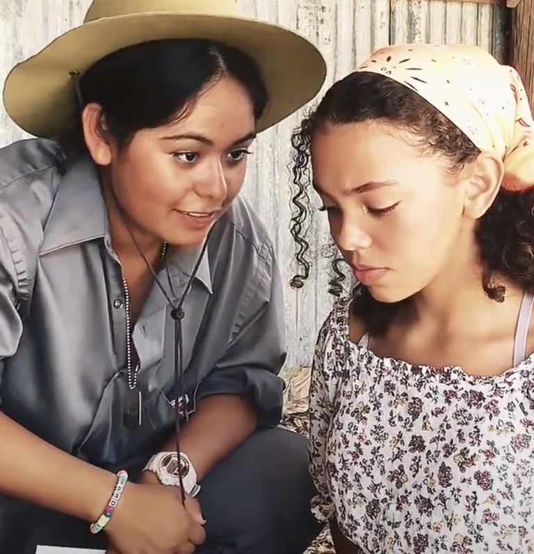 a young woman in a sheriff hat speaking to and a teen girl in a head scarf
