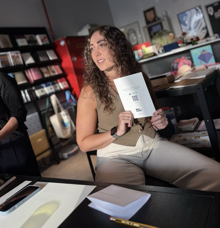 Judy sits in a bookstore holding up a designed card