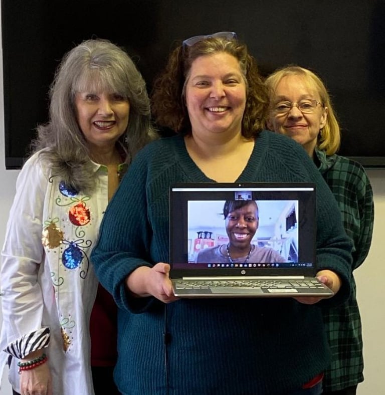 a woman holding a laptop computer and smiling with two more women behind her