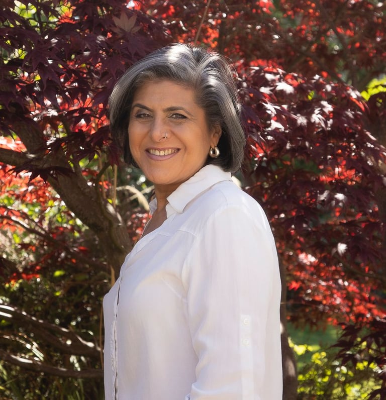 Smiling woman with short salt and pepper hair posing in front of a red Japanese maple tree.
