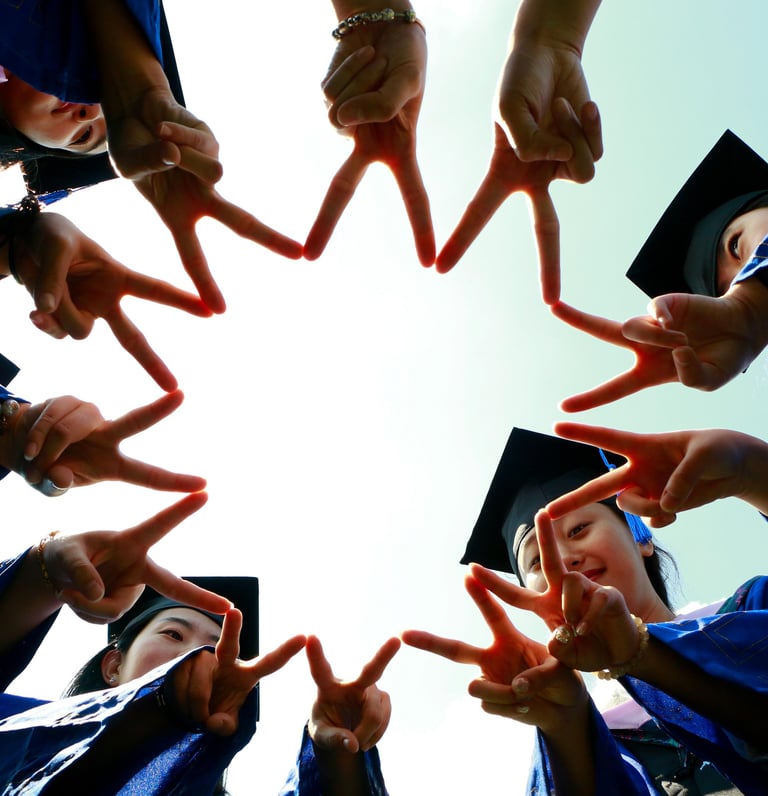 Group of graduates in blue gowns and caps forming a star shape with their fingers while celebrating 