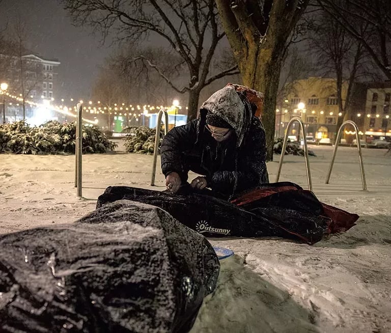 Man sitting in City Hall Park with his belongings in the snow.