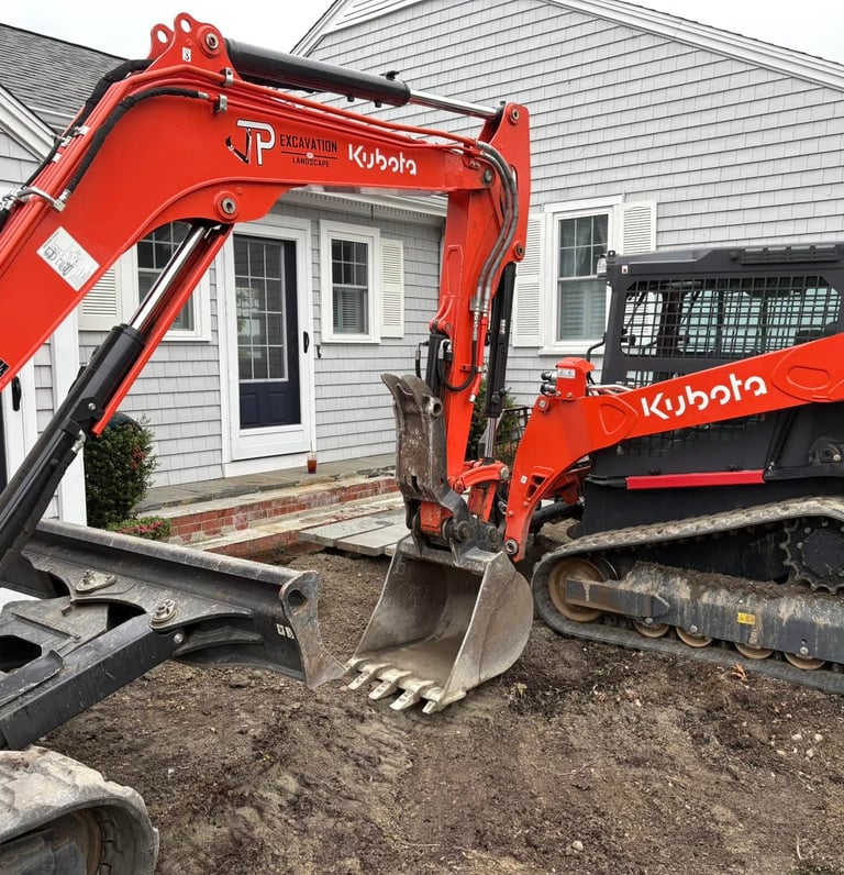 Orange Kubota SVL75-3 skid steer and excavator performing residential excavation and landscaping.
