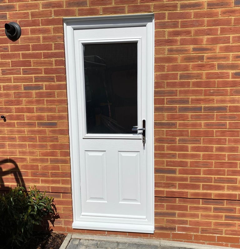 a white composite back door with chrome handle and half glazing on a red brick house.  It was fitted by buildmydoor
