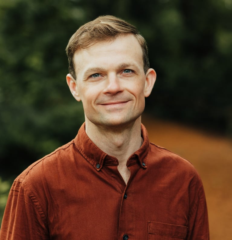 Headshot of Jesse Robertson wearing an orange collared shirt with a forested background.