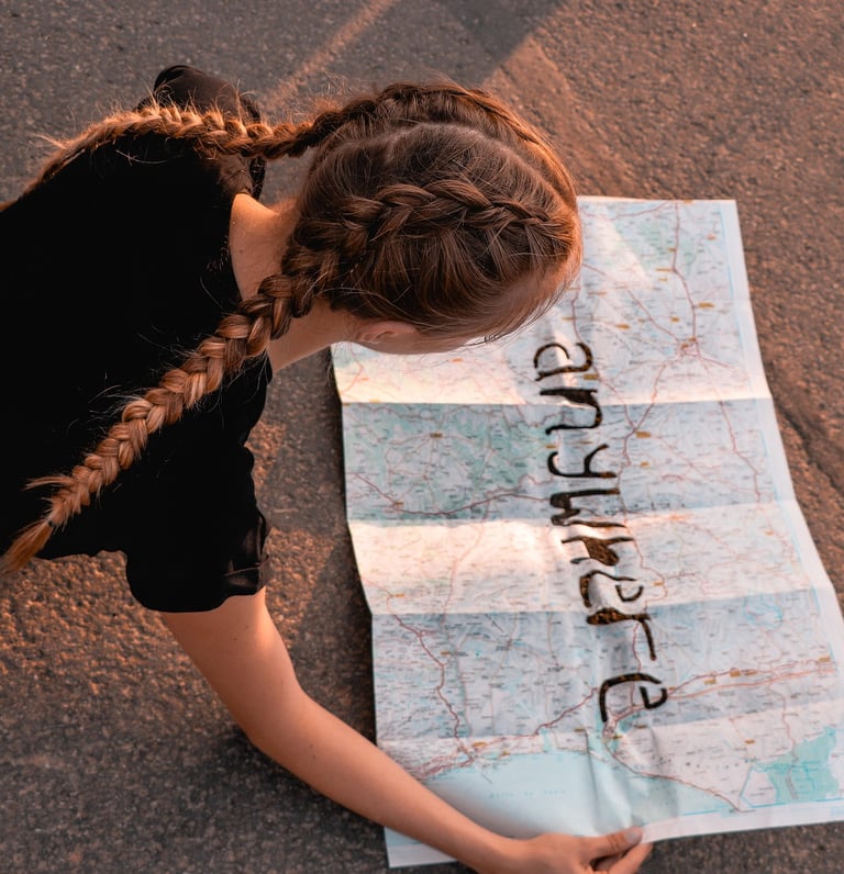 Young girl in braids laying down on road while she looks at map.
