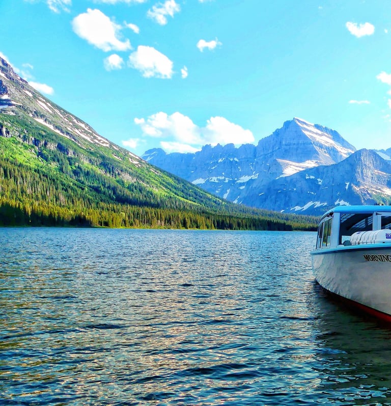 The Morning Eagle tour boat docked on a scenic lake in Glacier National Park with mountain views.