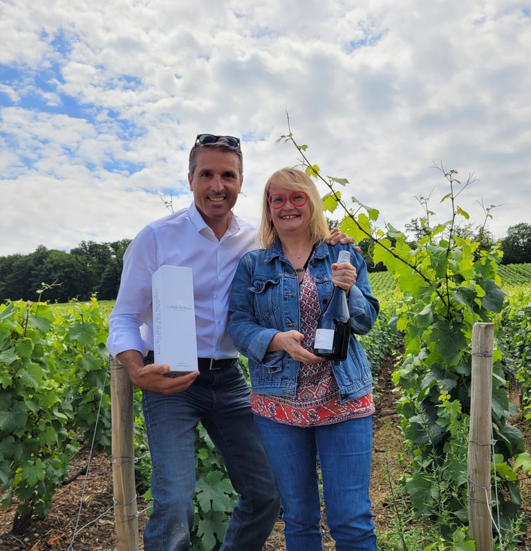 Patrice et Nathalie dans les vignes présentant la bouteille et l'étui du Champagne La Bulle du Bassi
