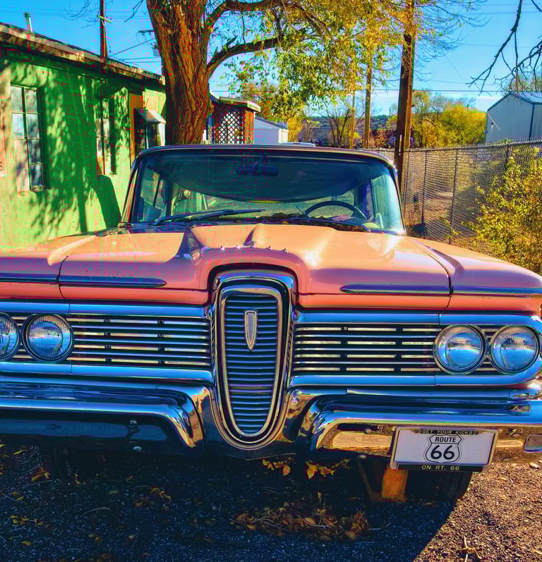 Vintage pink Edsel car with a Route 66 license plate parked outside a retro green building.