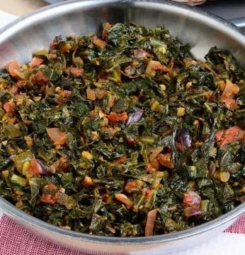 a frying pan filled with cooked collard greens, onions and tomato (gomen wat)