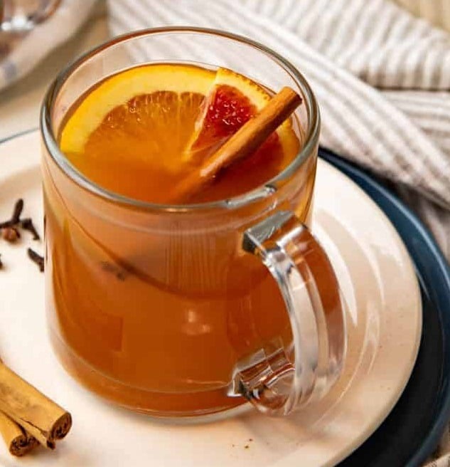 a clear glass mug filled with hot apple cider, orange slice and cinnamon stick garnish