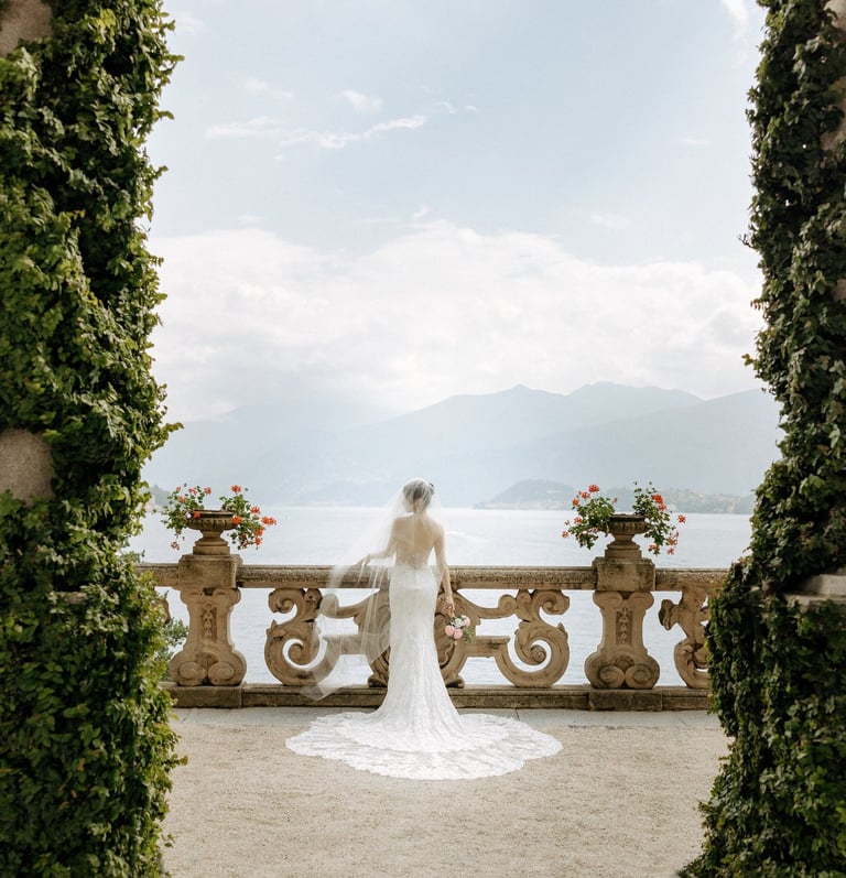 a bride in a white wedding dress standing in front of a lake at Villa Balbianello