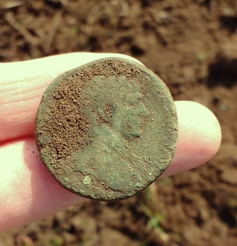 A large Roman coin with green patina, held out on two fingers of the finder.