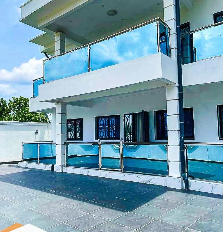 Villa de luxe moderne à Yaoundé avec façade blanche et balcons en verre teinté bleu.