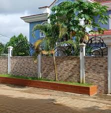 Mur de clôture en pierre avec grille en fer forgé noir et palmiers à Douala