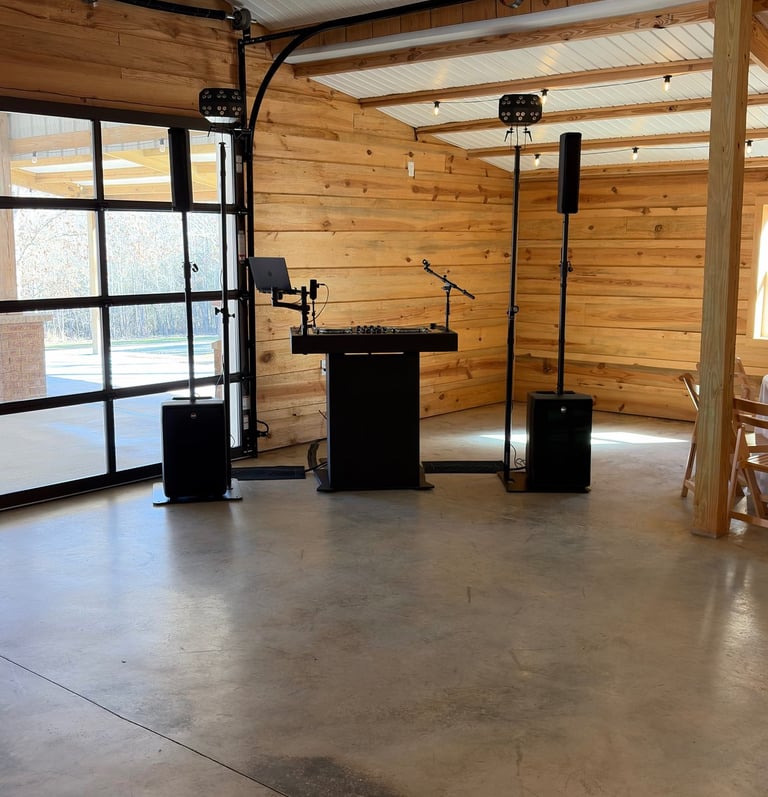 Professional DJ setup with a black booth, speakers, and blue party lights in a rustic wooden venue.