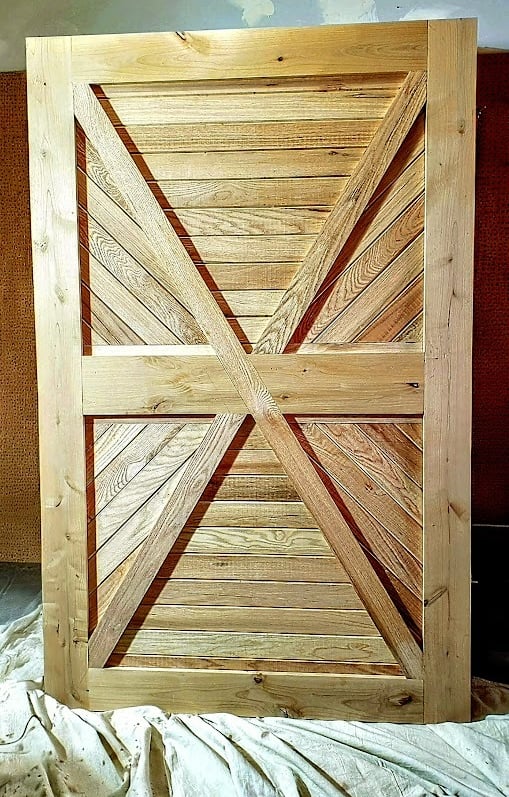 Handcrafted rustic sliding barn door made of light natural wood with a double X-brace design.